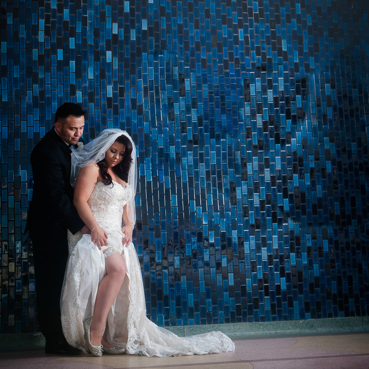Groom Lifting dress to see brides garter in front of blue tile wall